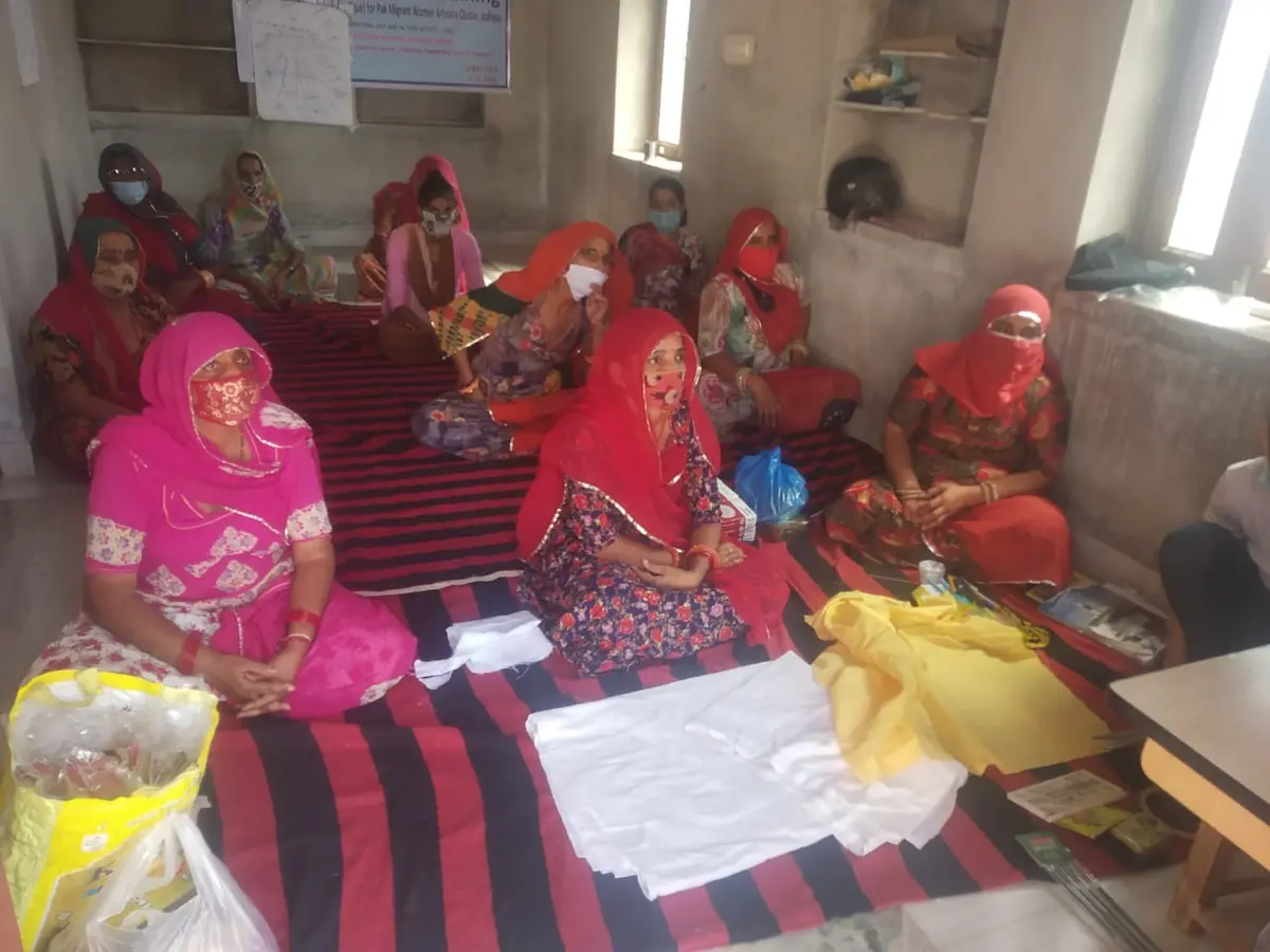 Artisans of the Pak Migrant Women Artisans Cluster gathered for a training round, project banner on the wall behind them.