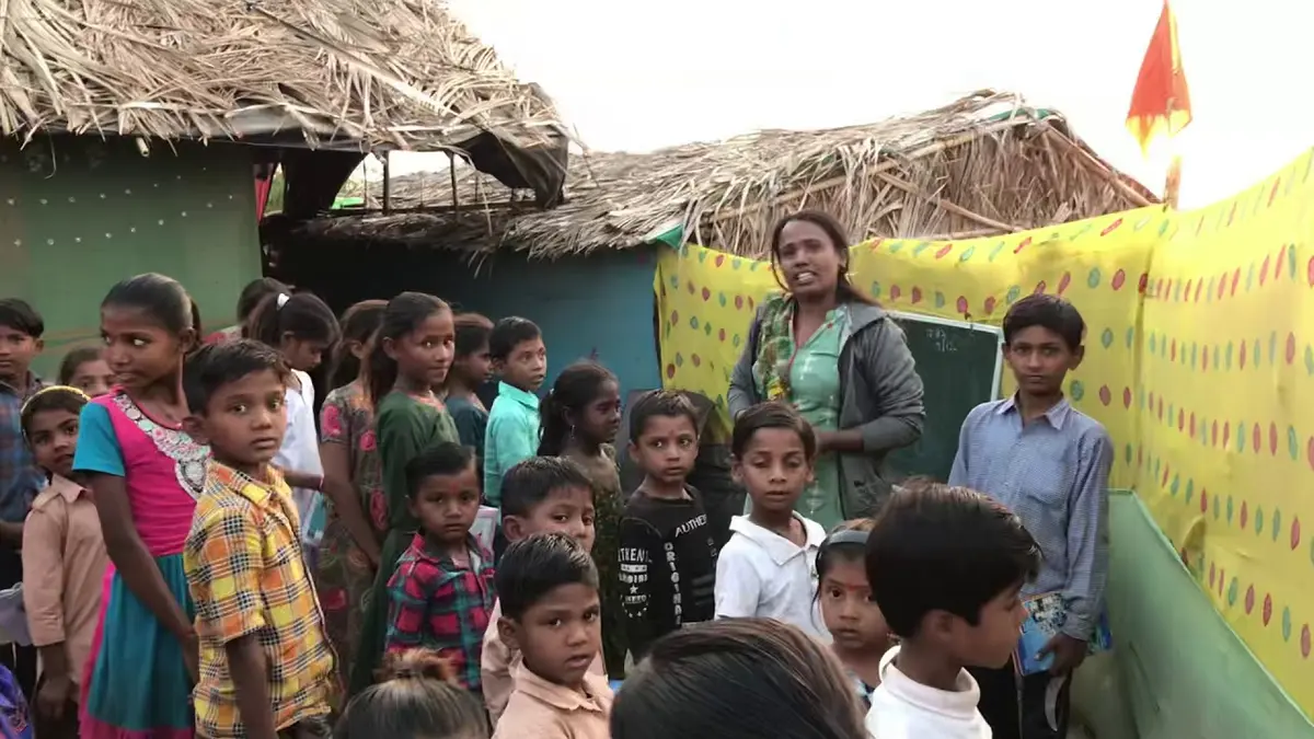 An outdoor lesson at the settlement, children gathered around their teacher.